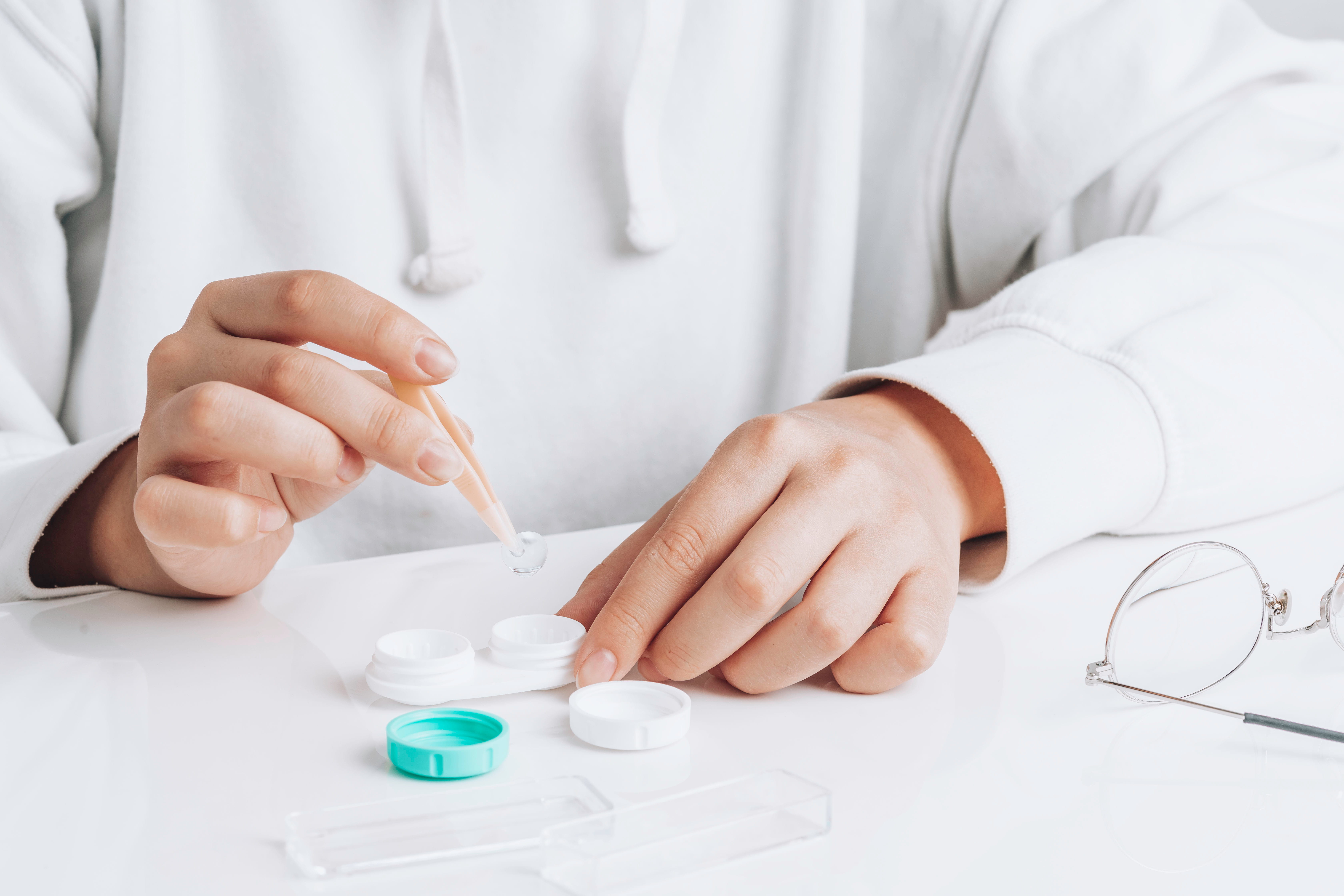Doctor in white coat handling contact lenses with tweezers near lens containers and glasses
