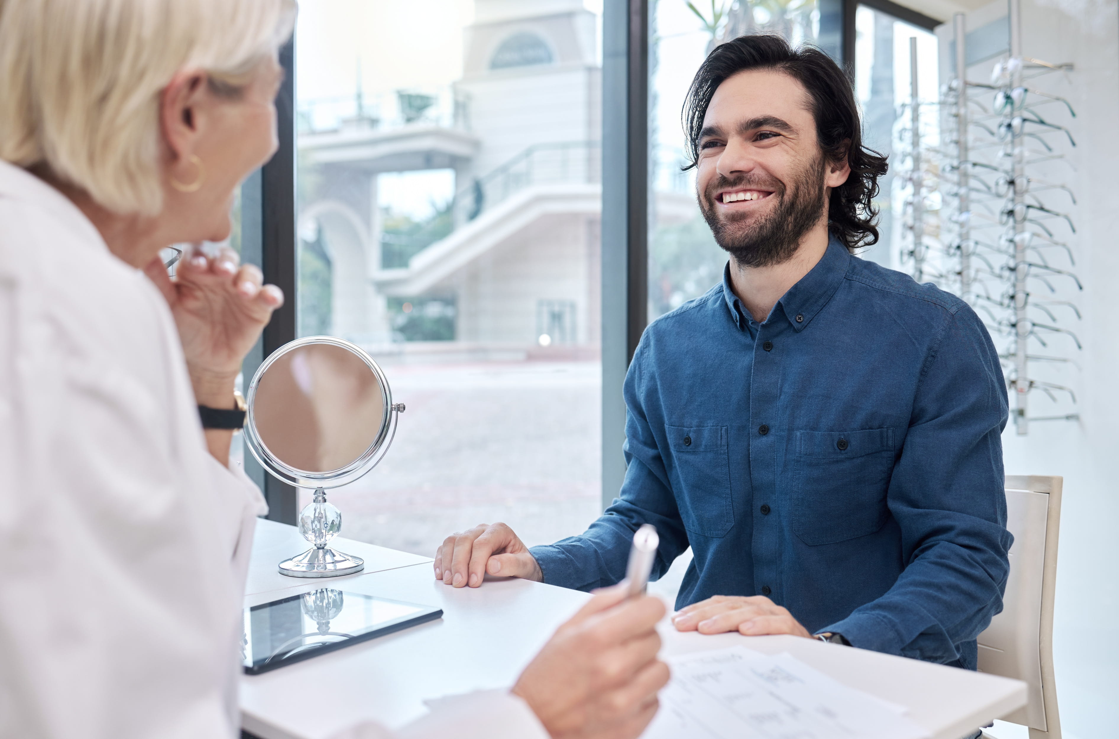 Optometrist showing female patient mirror during eye examination in bright modern office