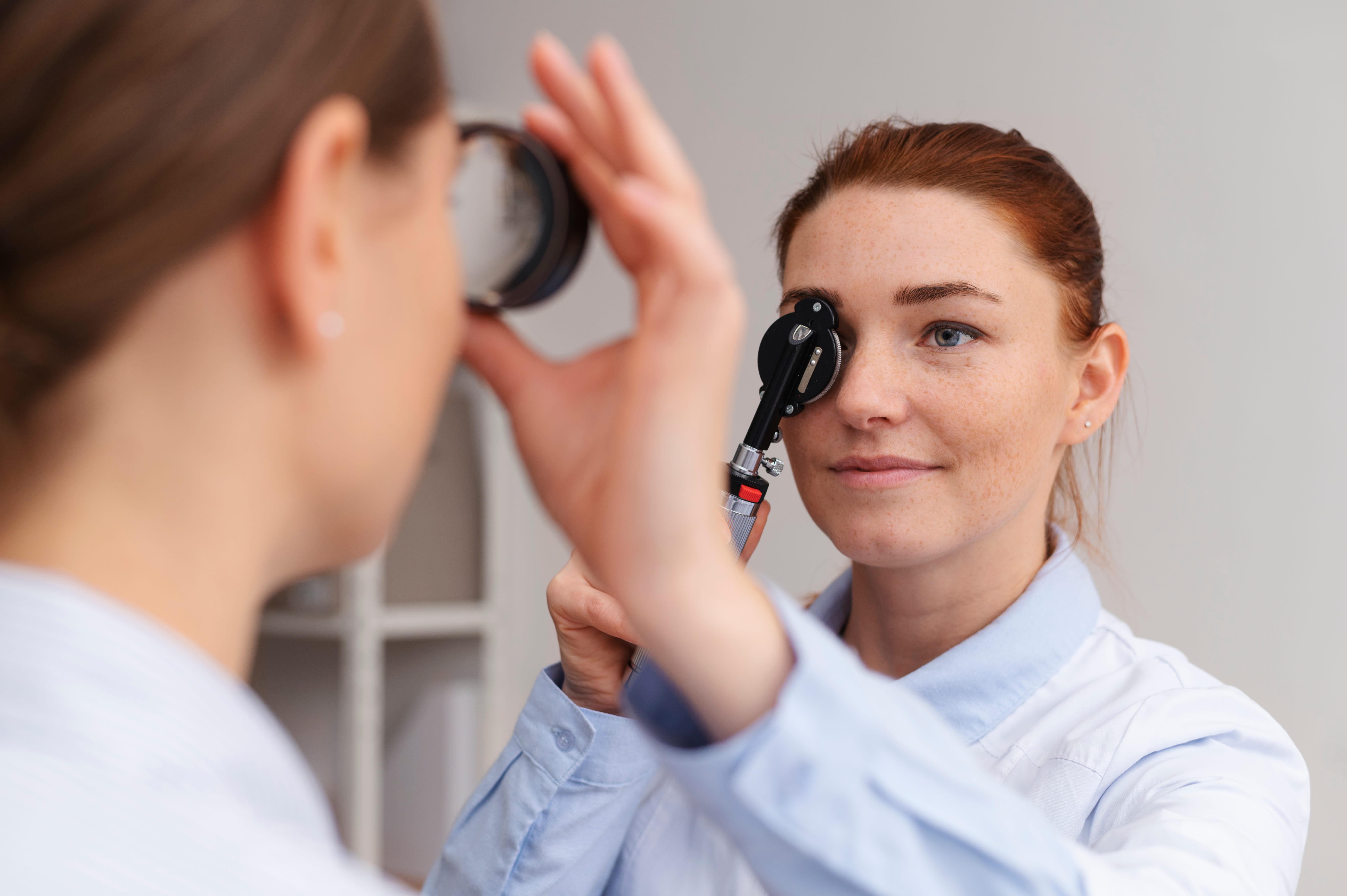 Female doctor using an ophthalmoscope to examine a patient's eye in a medical office.