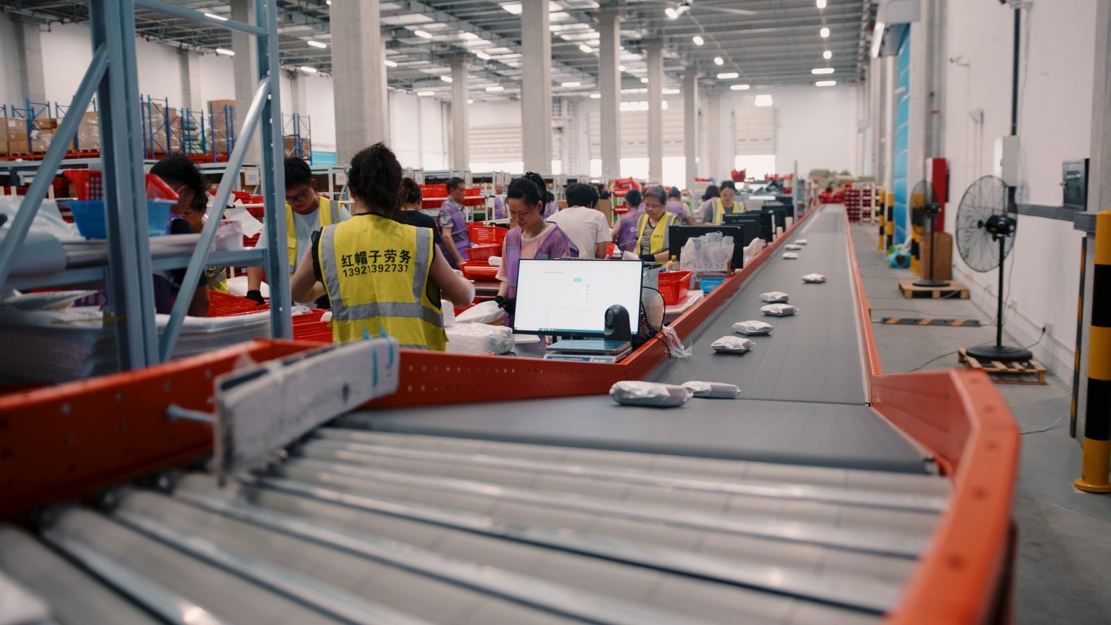 Parcels moving along a sorting conveyor while staff pack orders on the warehouse floor