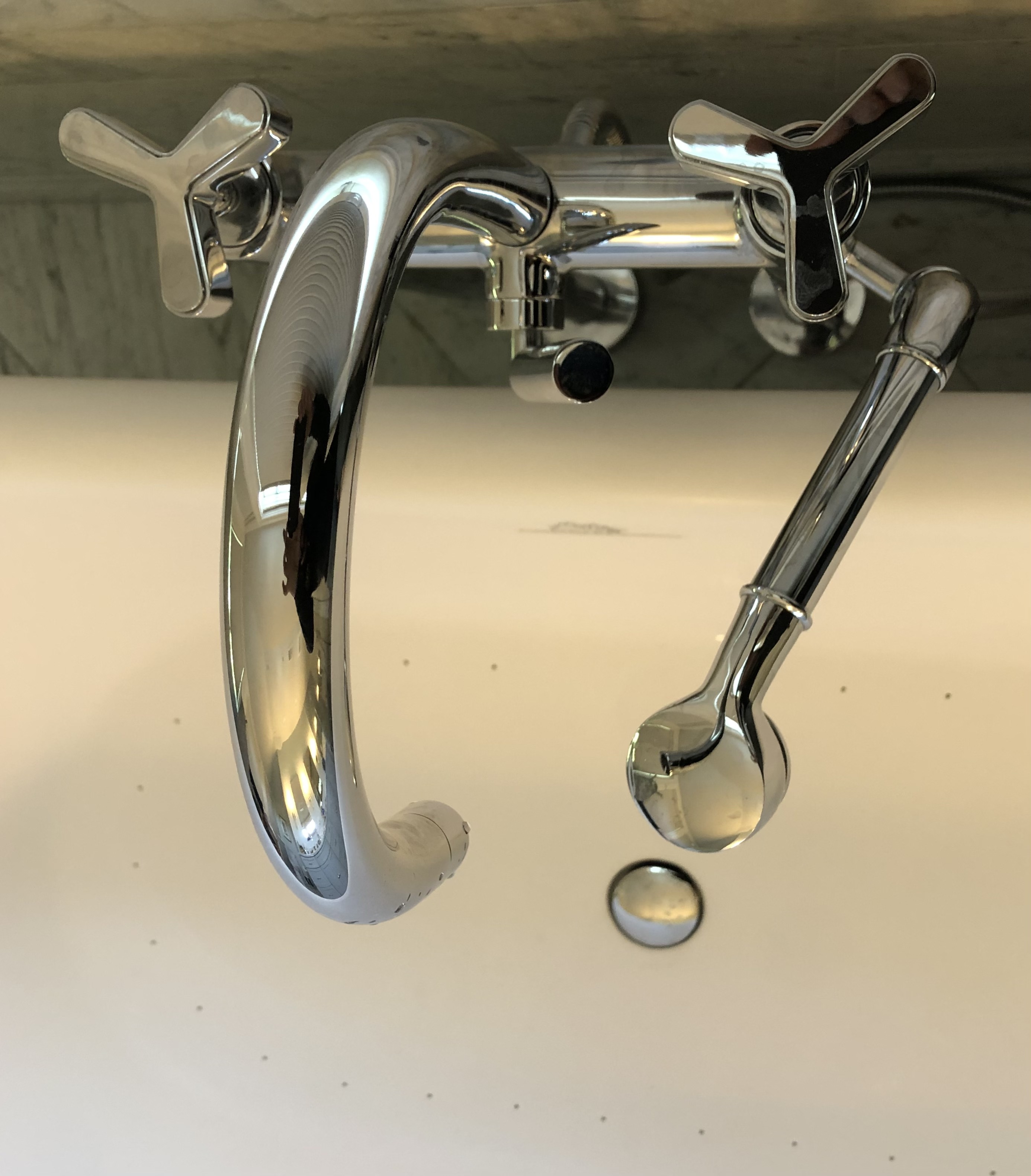 A modern bathroom featuring a glass-enclosed walk-in shower with rain showerhead on the left, a streamlined white toilet centered under a window, and a floating wooden-topped vanity with two vessel sinks and chrome faucets on the right.