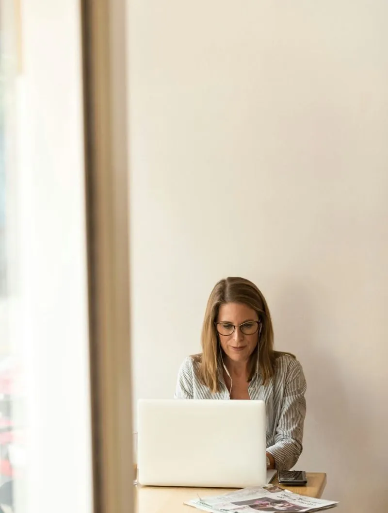 woman wearing grey striped dress shirt sitting down near brown wooden table in front of white laptop computer