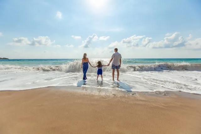 A man, a woman and child holding hands on seashore