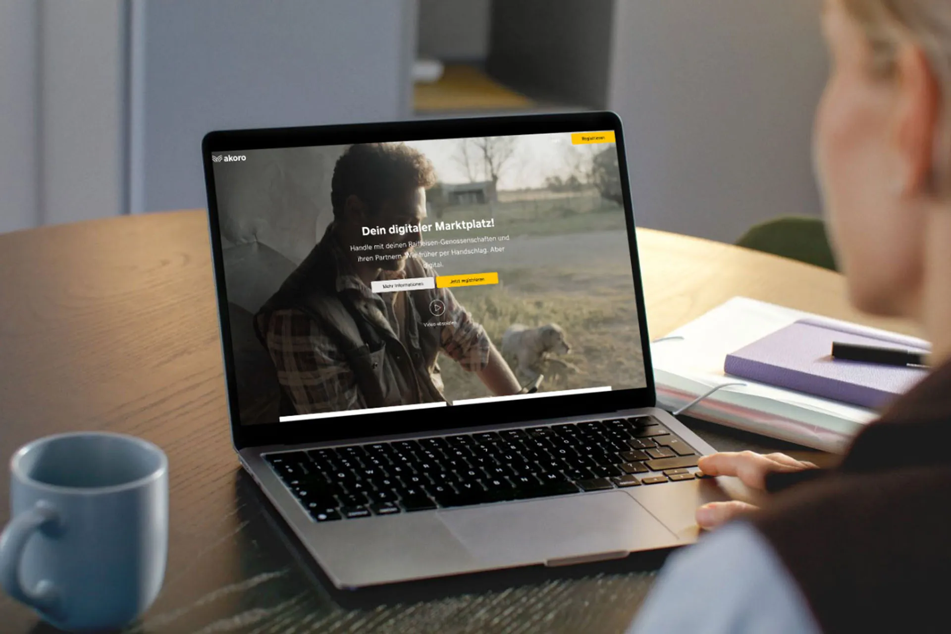 Eine Person sitzt an einem Tisch und arbeitet an einem Laptop, auf dessen Bildschirm eine Webseite mit Login-Möglichkeit geöffnet ist.
