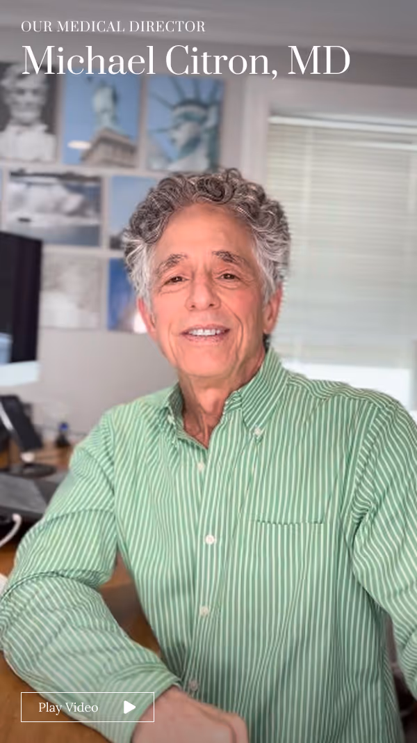 Smiling man with curly gray hair wearing a green striped shirt sitting in an office.