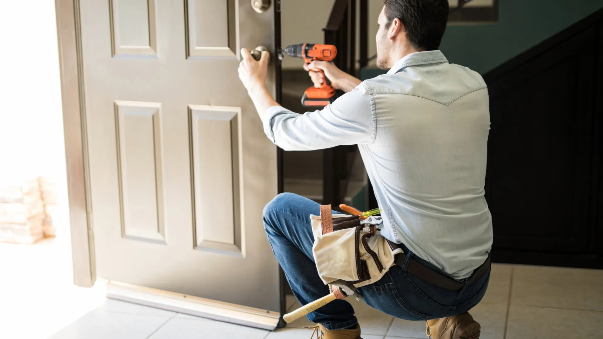 Handyman using a power drill to install a lock on a white interior door