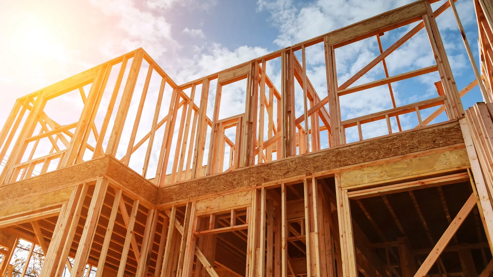 New home wood framing rising against a bright blue sky with sunlight and white clouds