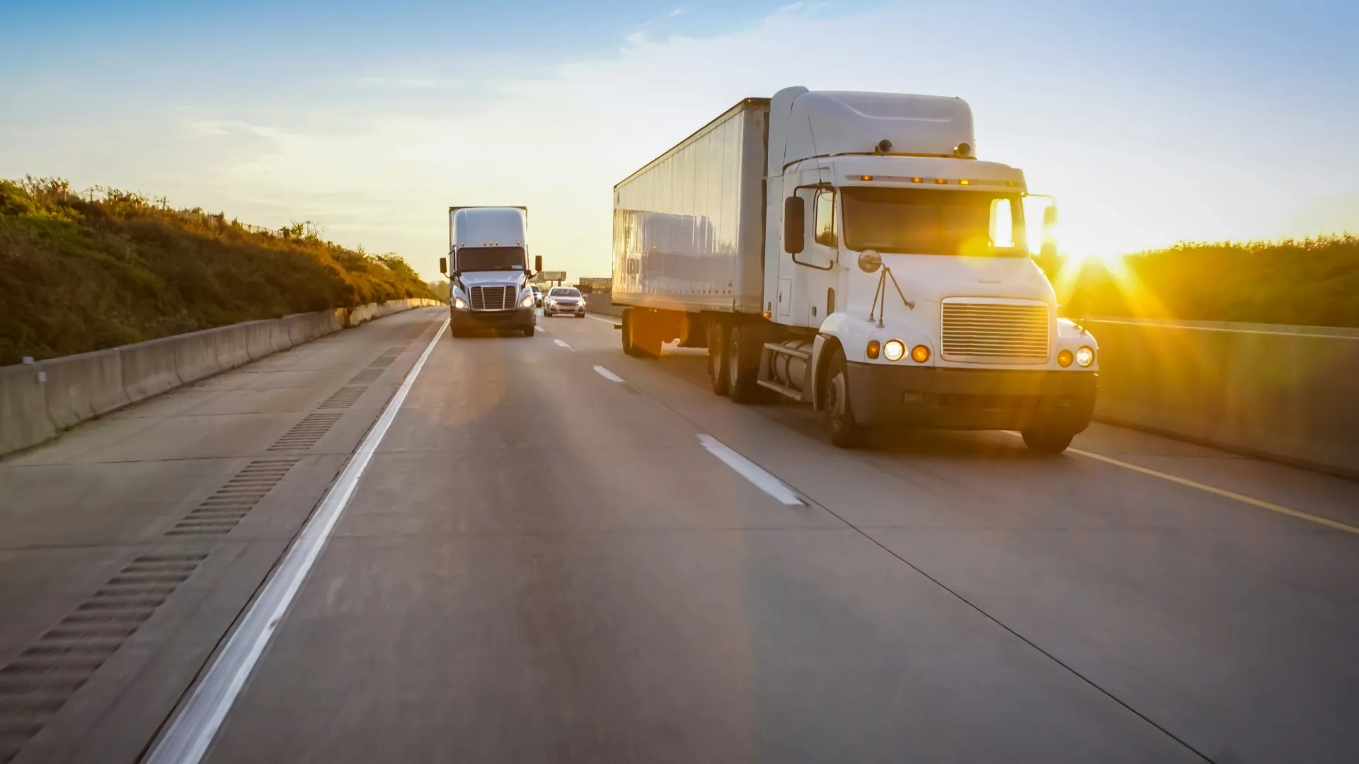 Two semi trucks driving down a highway toward the camera at sunset