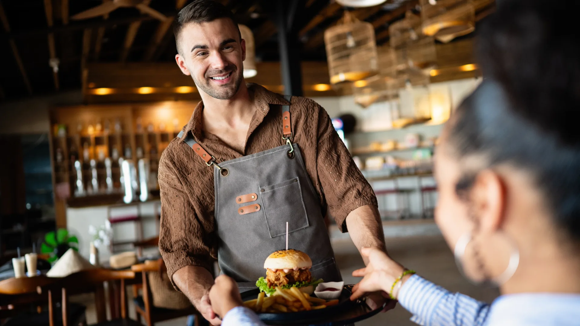 Server bringing a burger and fries to a table in a relaxed restaurant