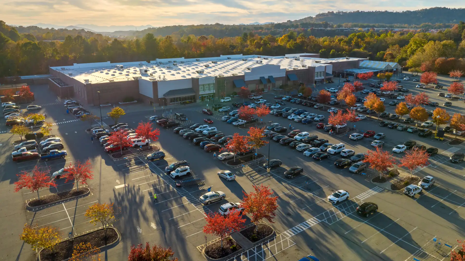 Aerial view of a shopping center anchored by a grocery store, with a full parking lot and autumn trees