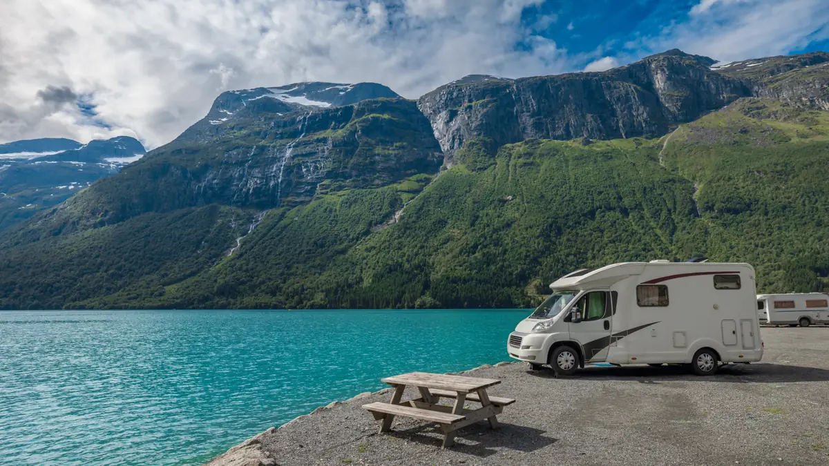 Motorhome parked beside a turquoise lake below mountains