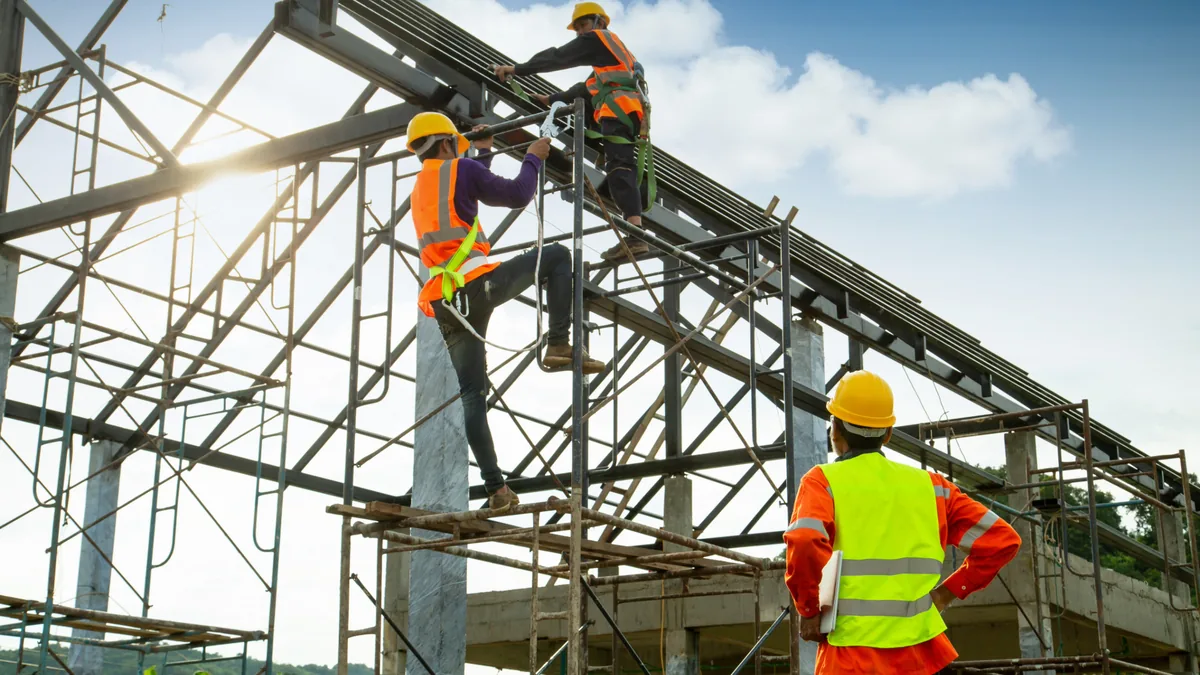 Worker in a safety harness building a steel roof structure under a blue sky