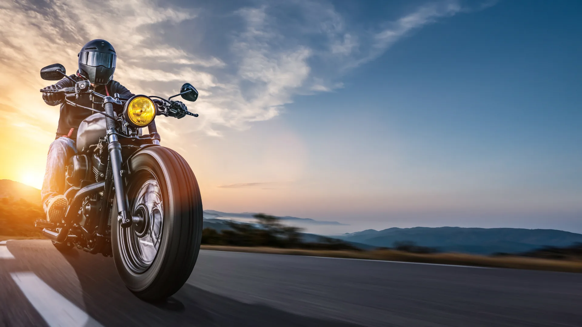 Motorcycle rider on an open coastal road under a dramatic blue sky