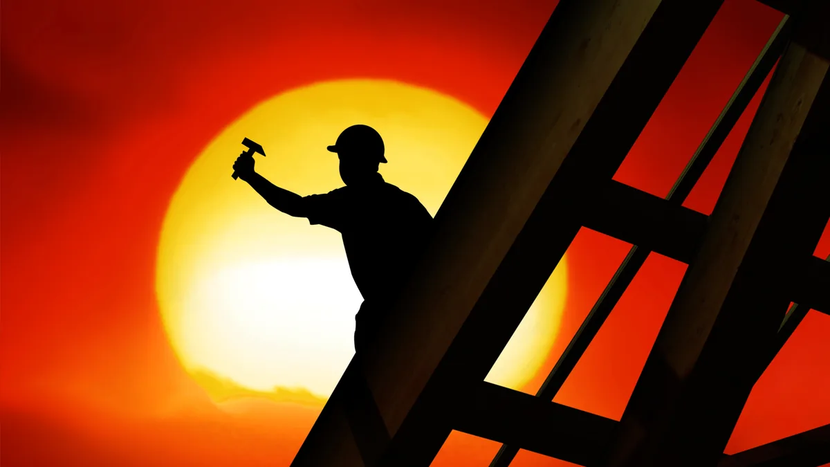 Roof worker silhouetted against a huge red-orange setting sun