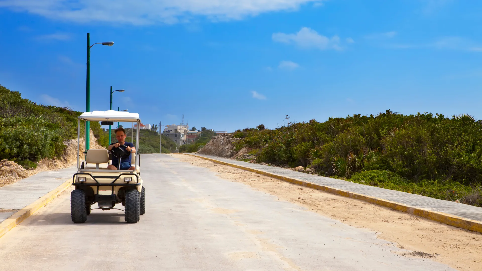 Man driving a golf cart along a sunny coastal road