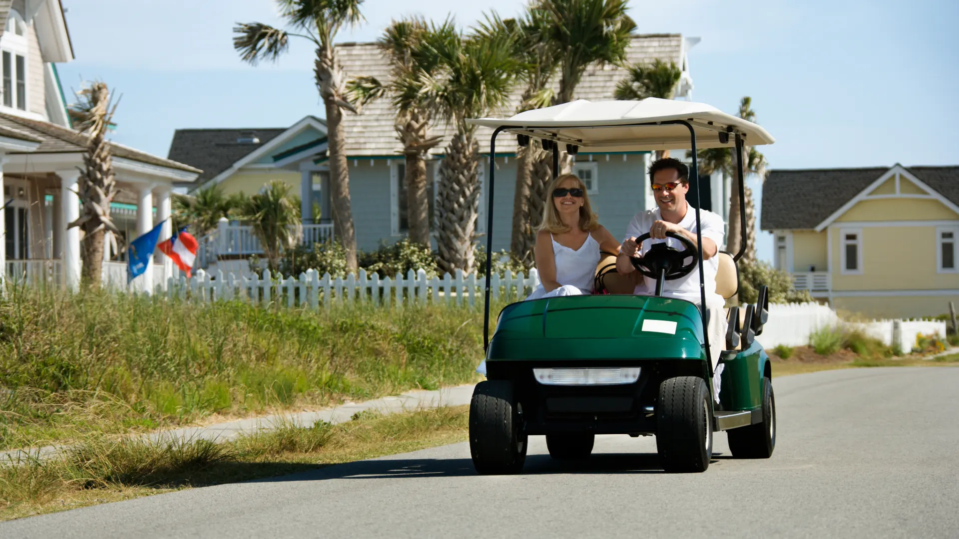 Couple driving a golf cart down a neighborhood street lined with houses