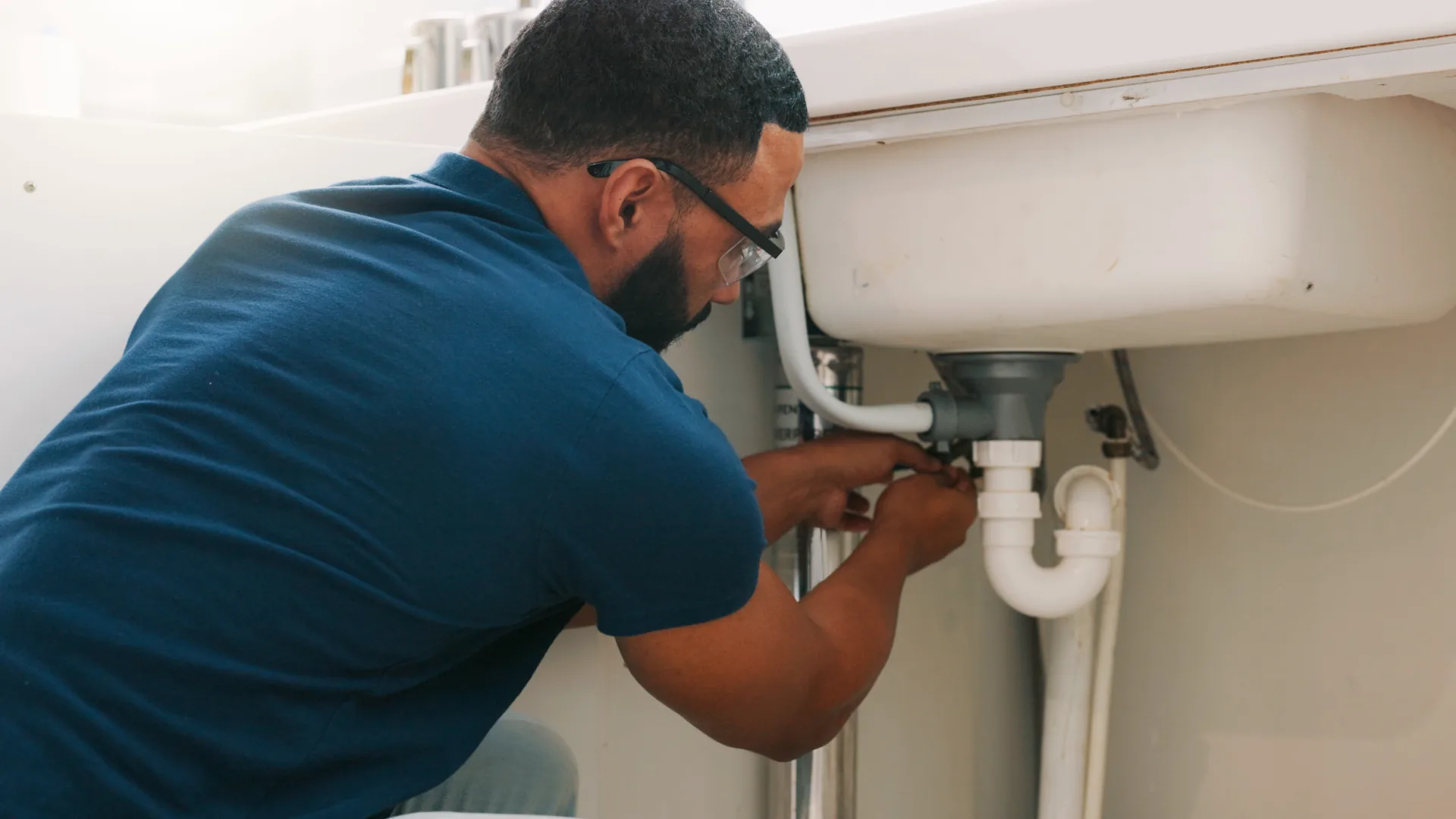 Plumber repairing the pipes under a sink with tools
