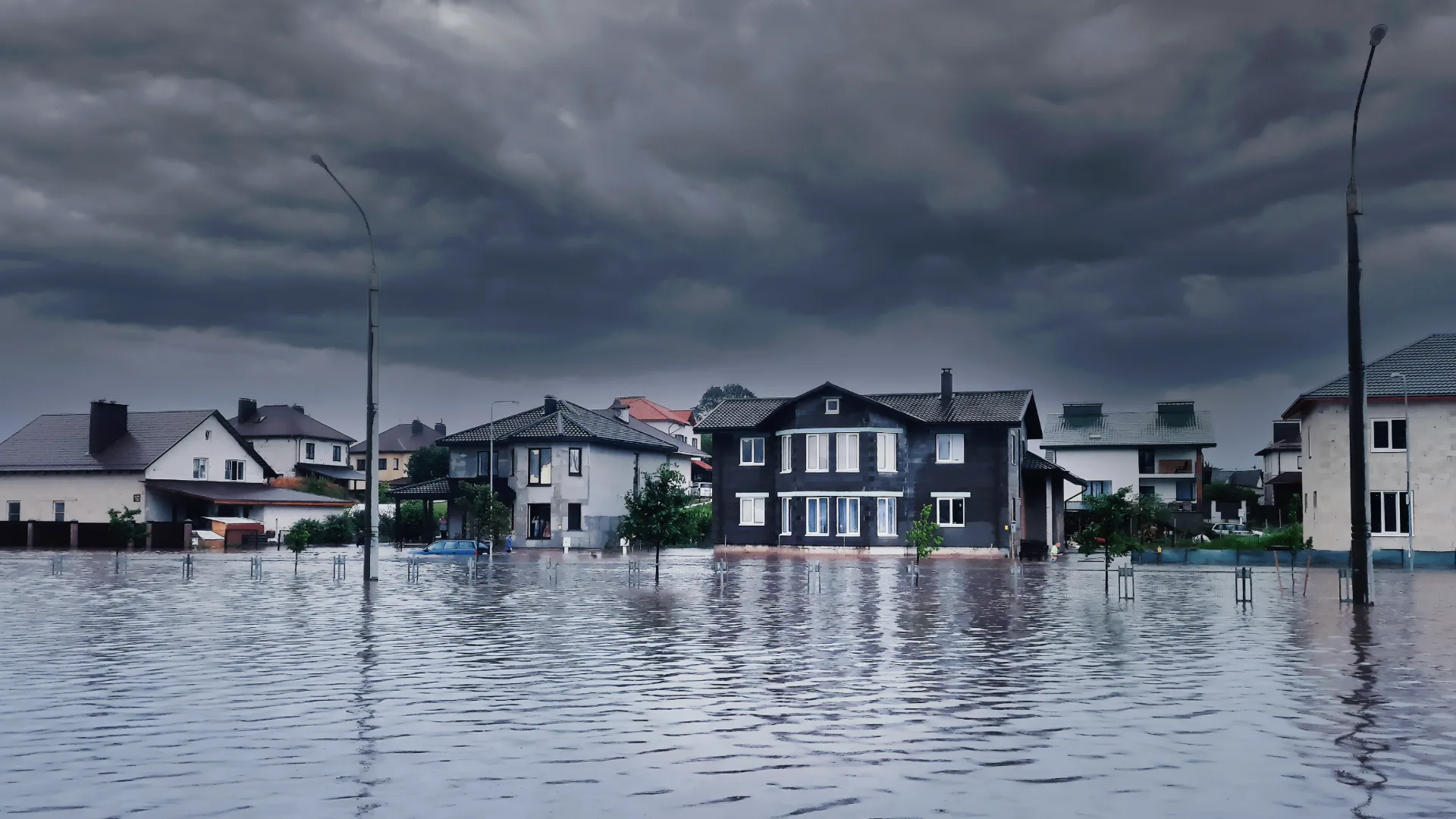 Floodwater covering a neighborhood street under dark storm clouds