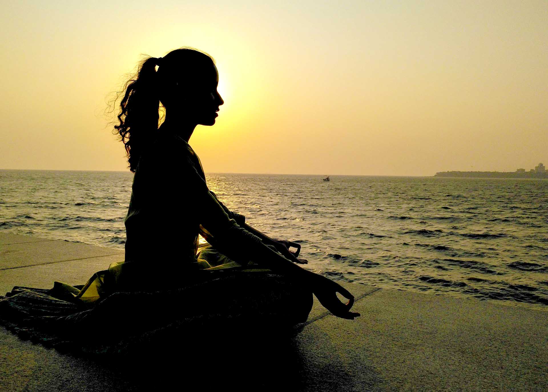 Frau praktiziert eine geführte Meditation von om vibes only bei Sonnenuntergang am Meer