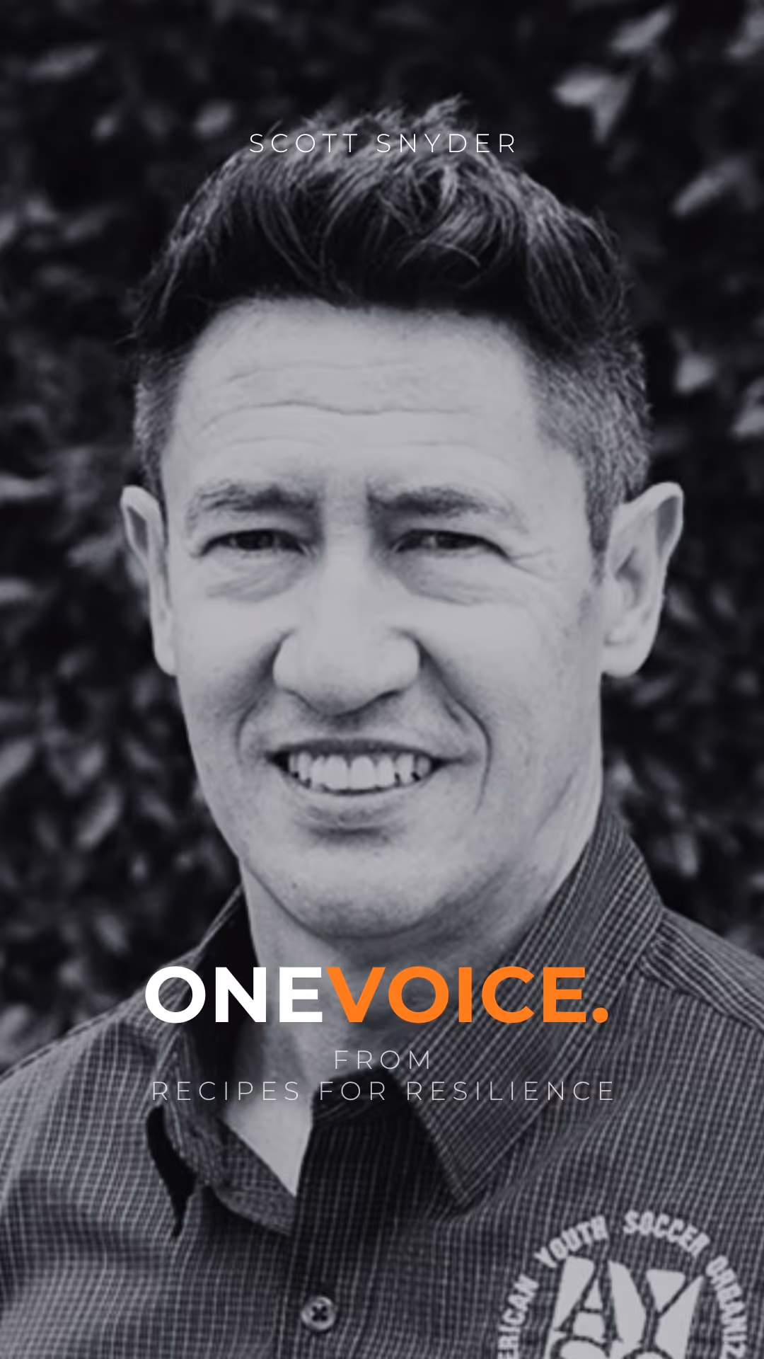 Black and white portrait of a smiling man with glasses and a beard wearing a suit and polka-dot tie in an elegant setting.