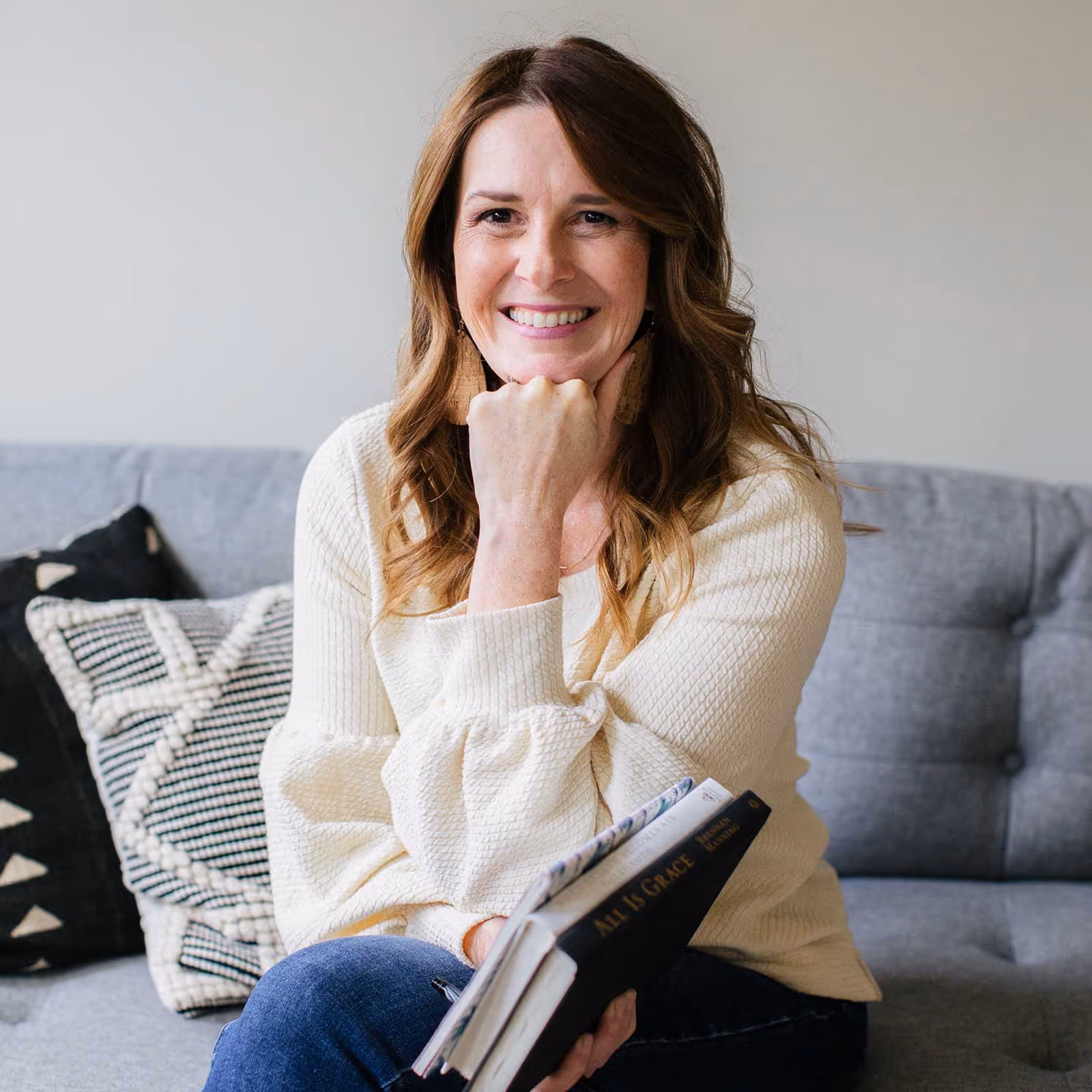Karla Osorno sitting on a grey couch with books in her hand