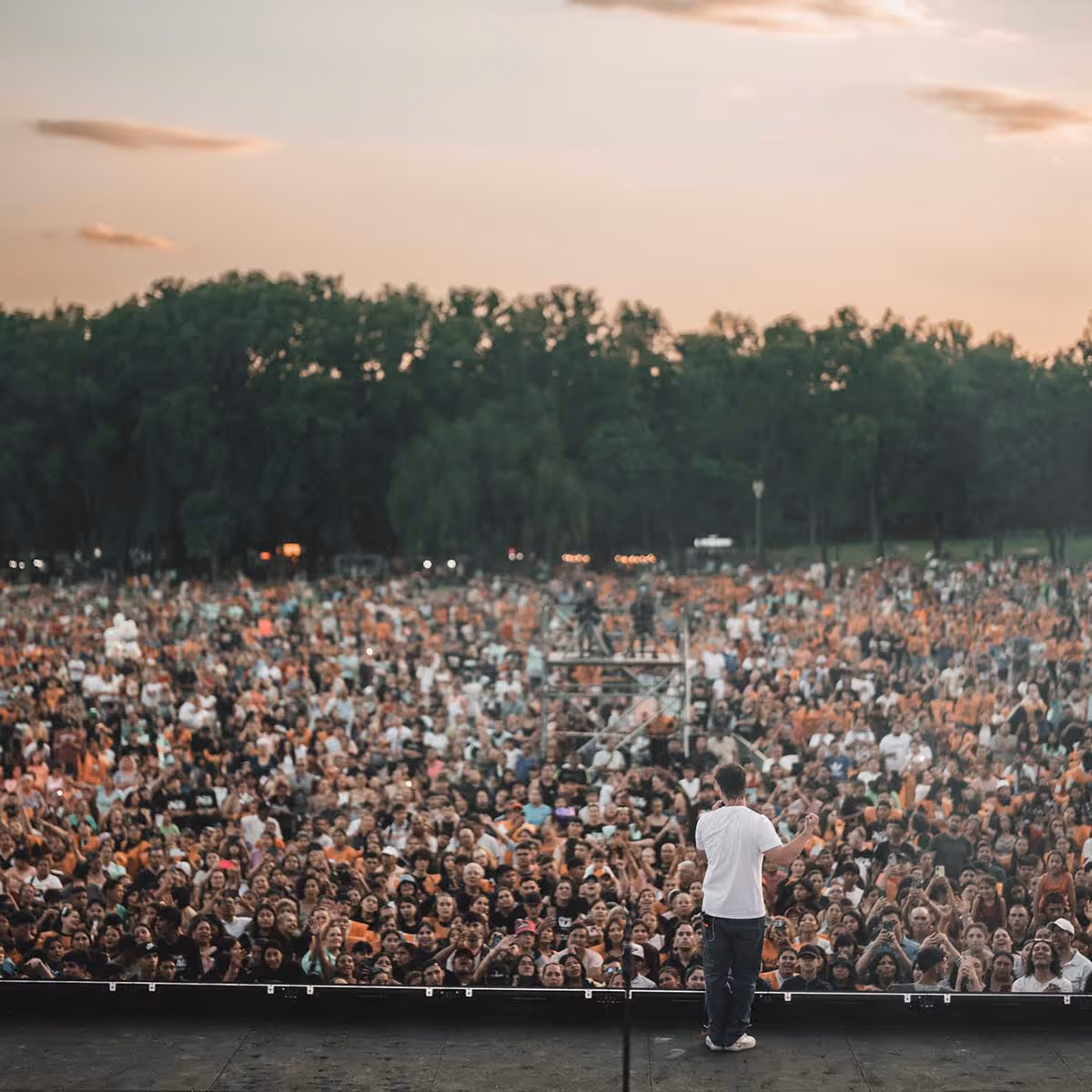 A man standing on stage speaking to a large crowd of people 