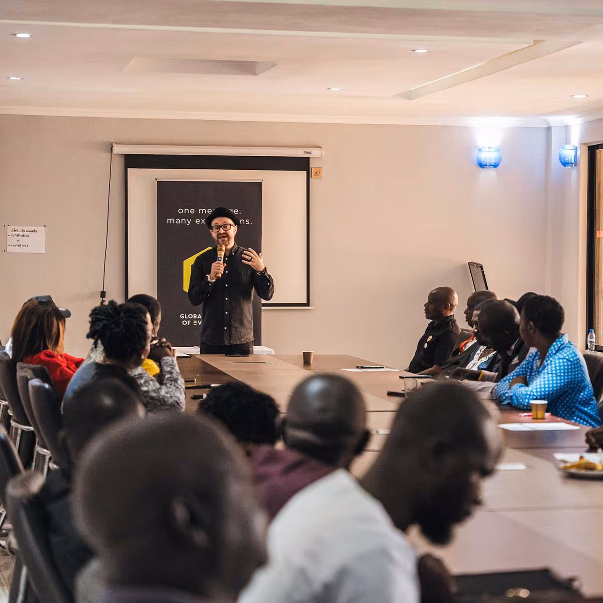 A man standing at the head of a conference table speaking to a room of people 