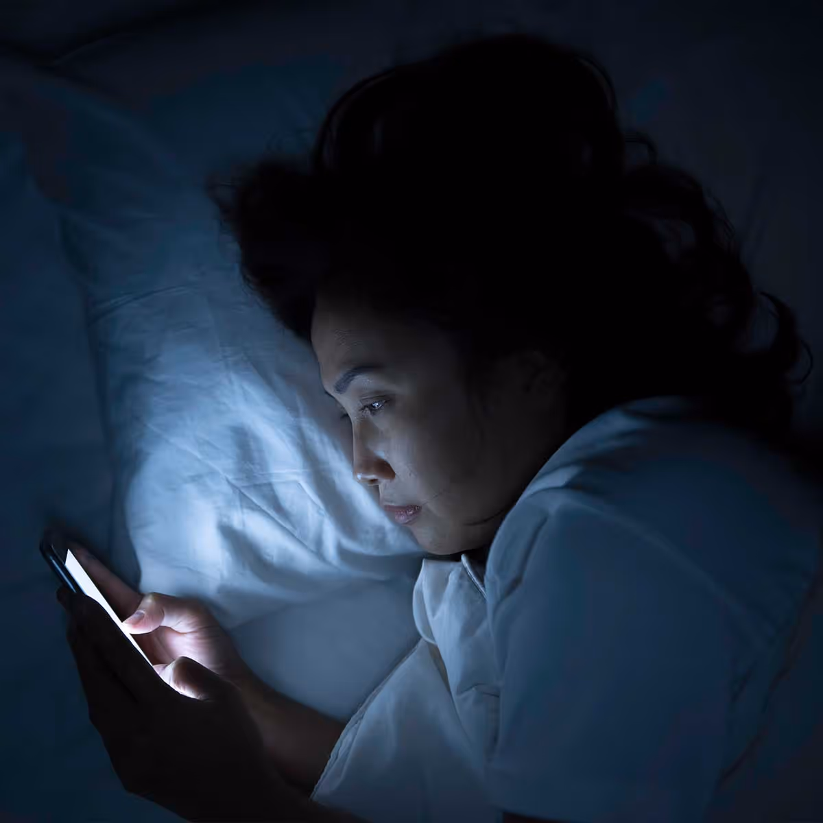 A woman in her bed on her phone at night 