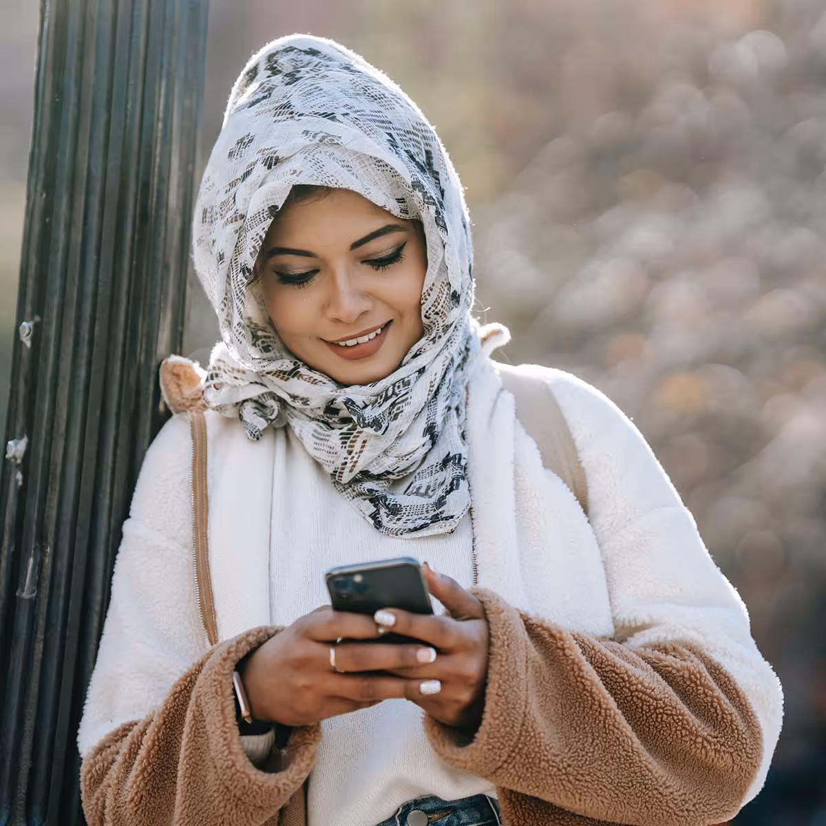 A woman leaning against a pole looking on her phone and smiling 