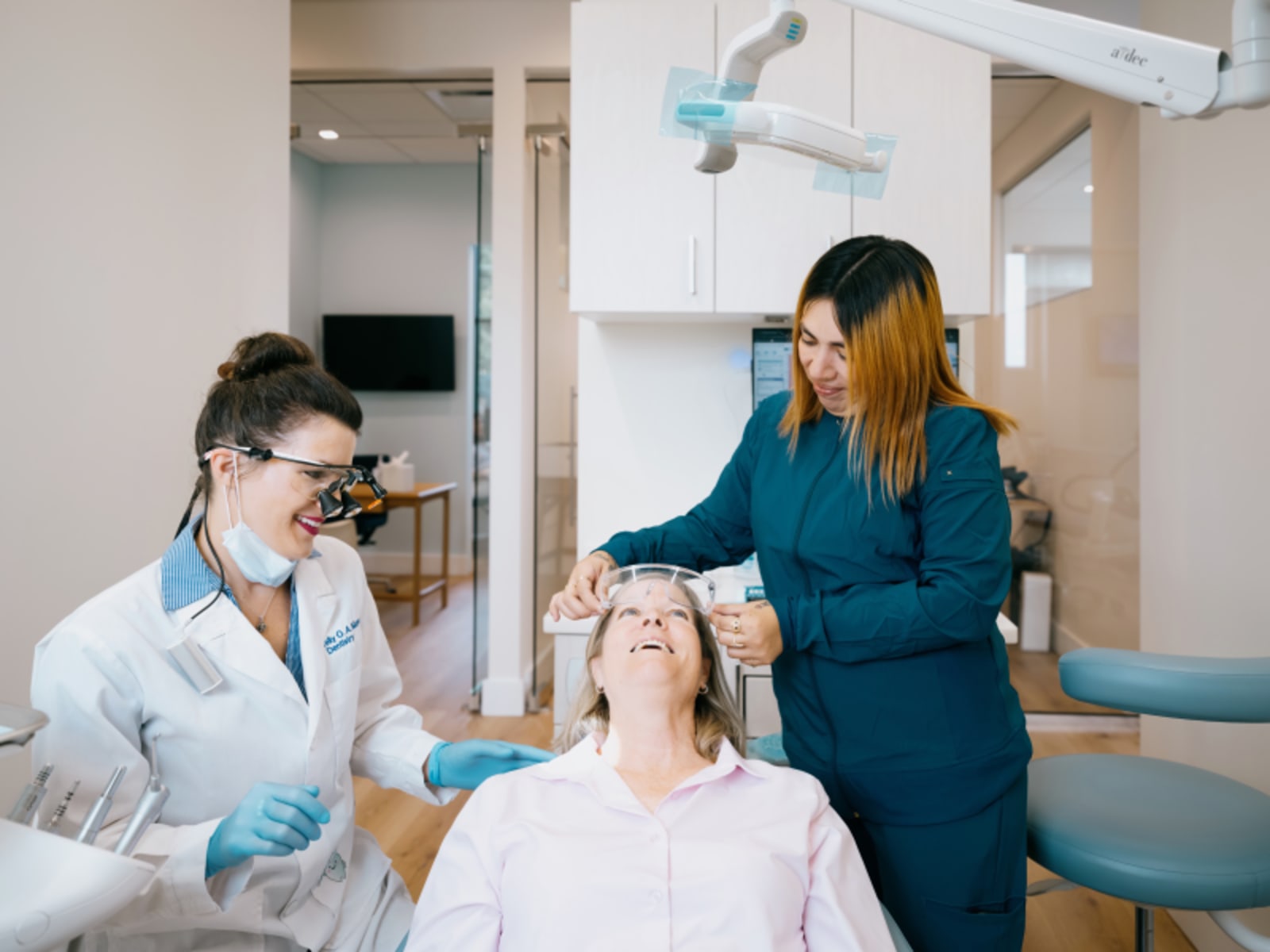 Female dentist in white coat and blue gloves performing clinical examination in treatment room