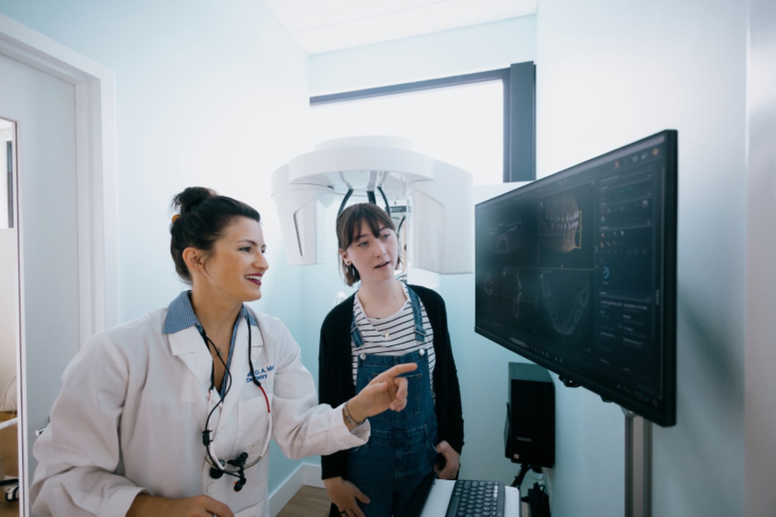 Dentist and assistant discussing treatment plan while reviewing digital scan with patient