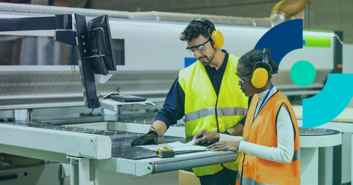 Two workers in hi-vis vests and ear defenders reviewing documentation on a manufacturing factory floor, representing workplace health and safety compliance in UK industry.