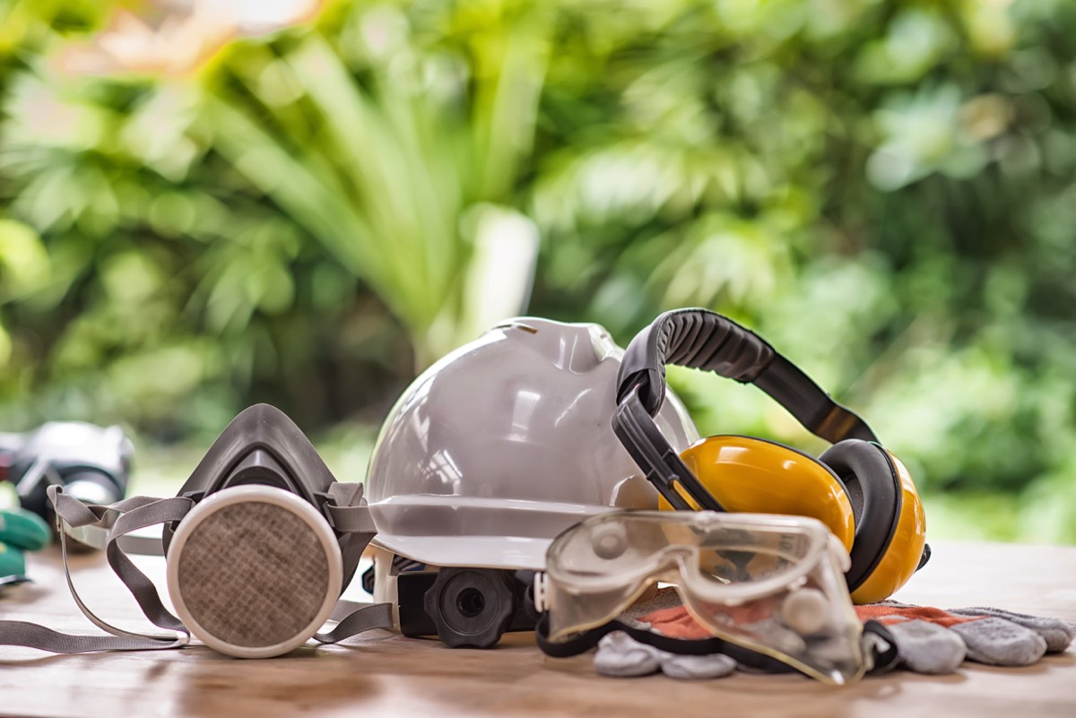 Personal protective equipment including hard hat, ear defenders, safety goggles and respirator mask on a work surface