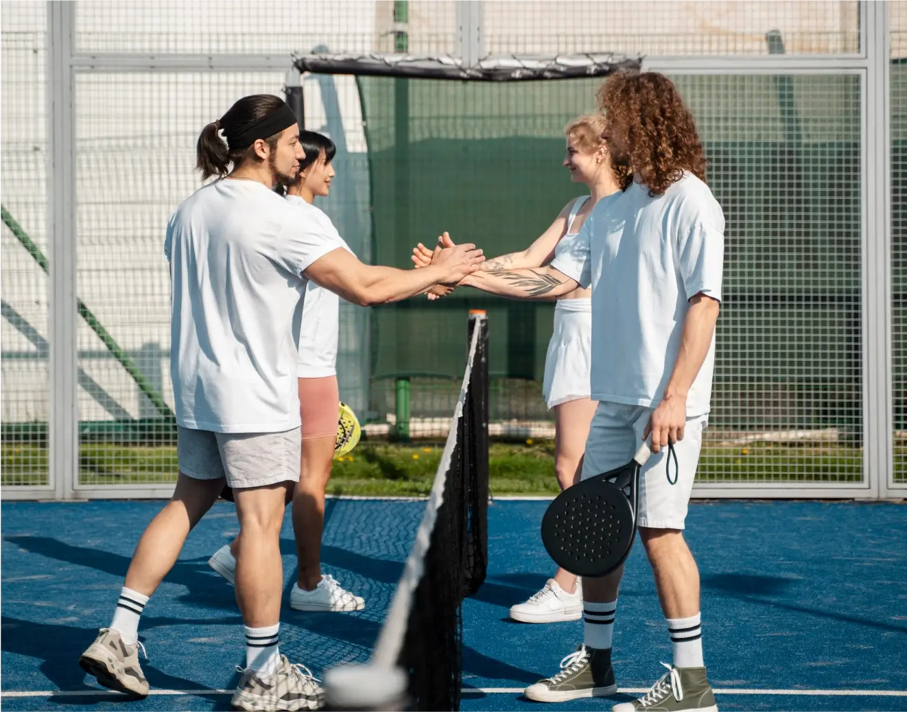 Four padel players shaking hands over the net after a match.