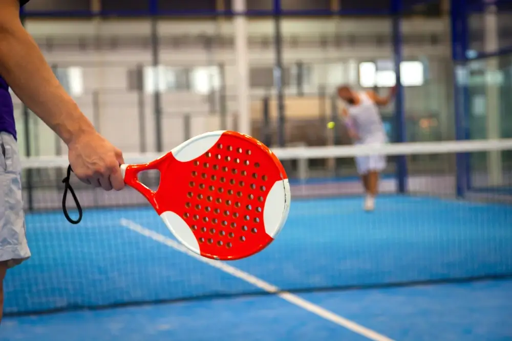 A red padel racket about to hit the ball.