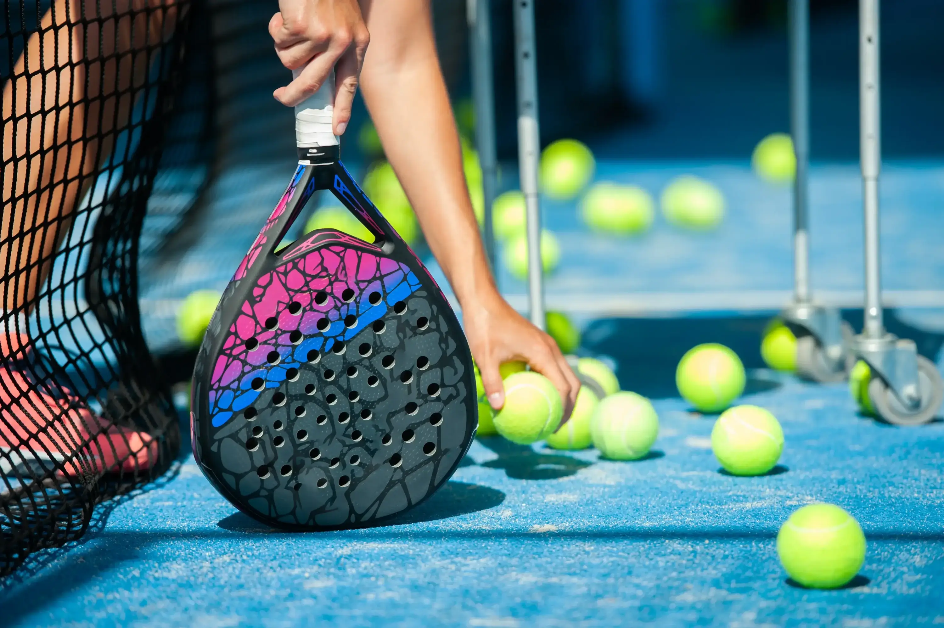 Padel player leaning over the net picking up balls.