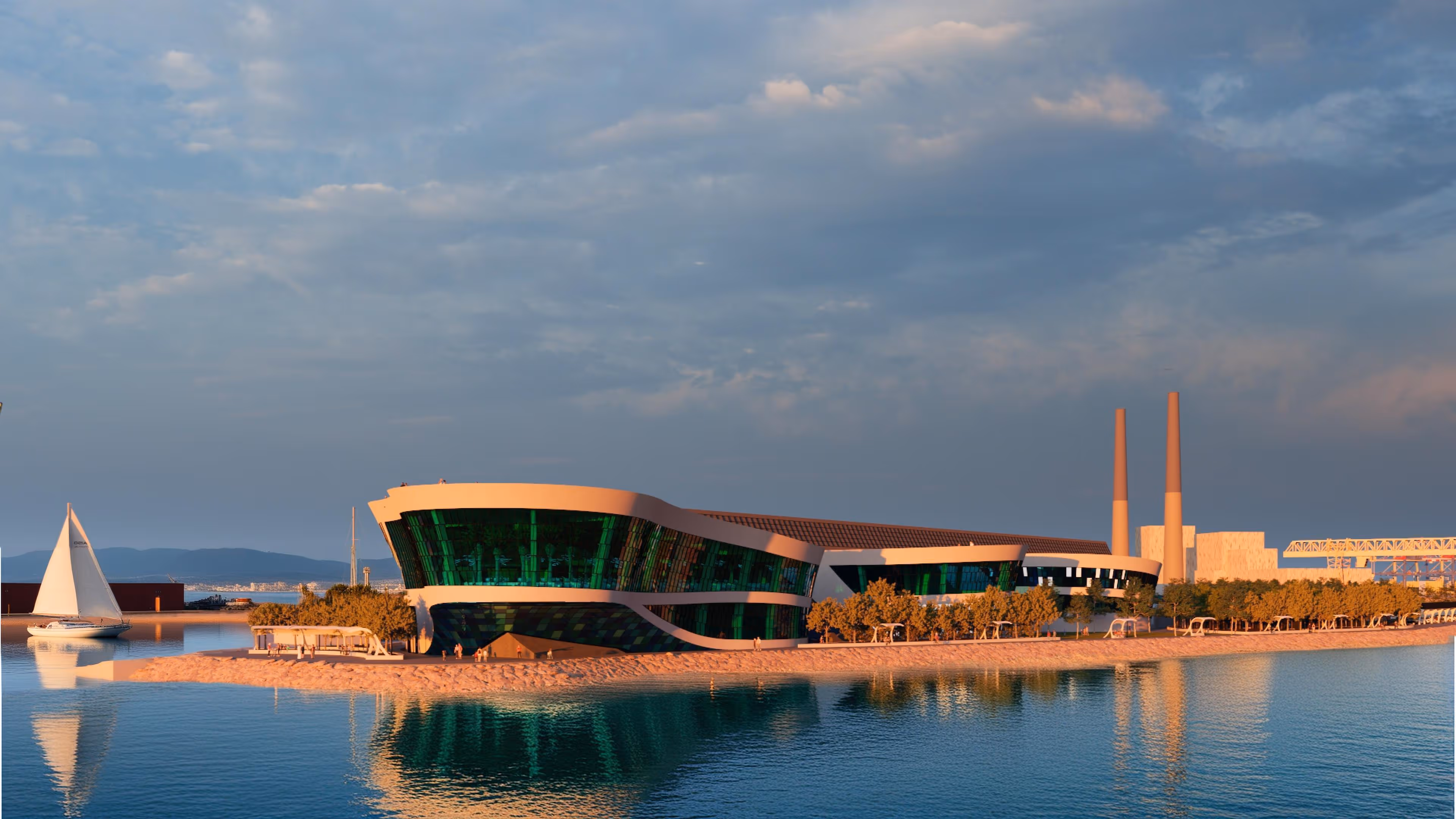Modern waterfront building with curved green glass facade beside a beach and sailboat on calm water at sunset.