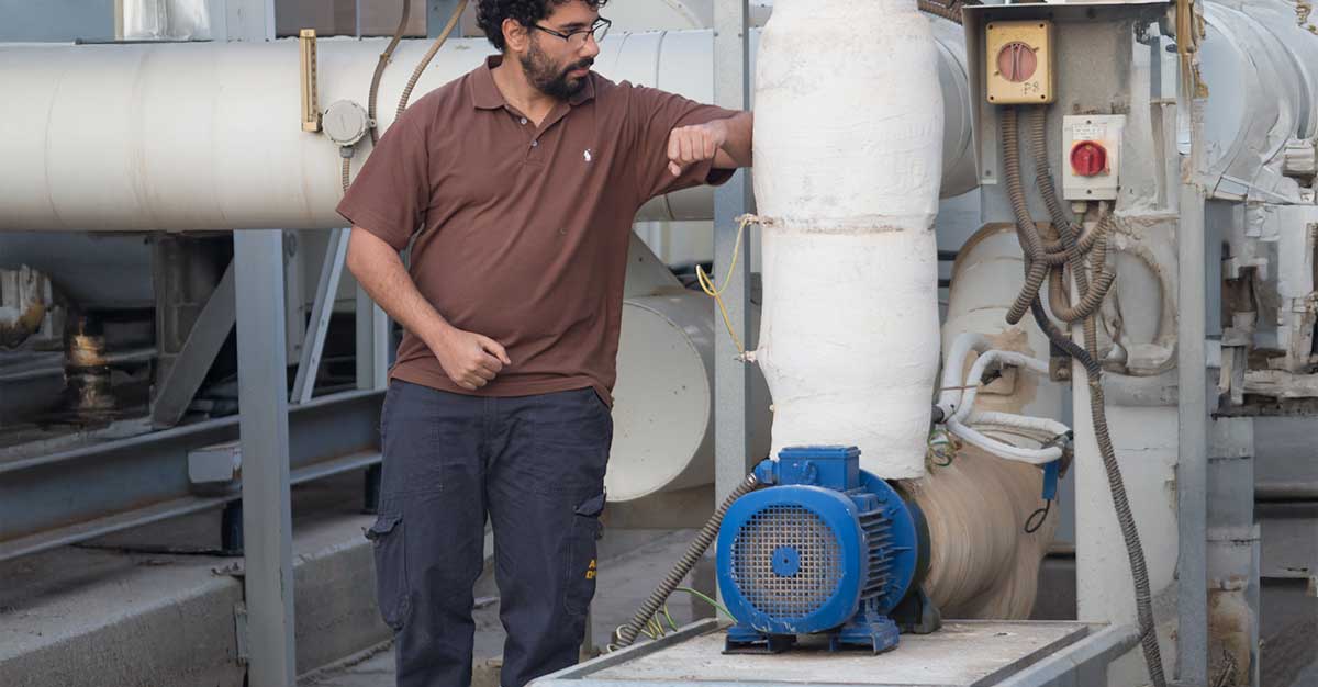 Technician inspecting industrial HVAC equipment with large insulated pipes and a motor unit at a facility.