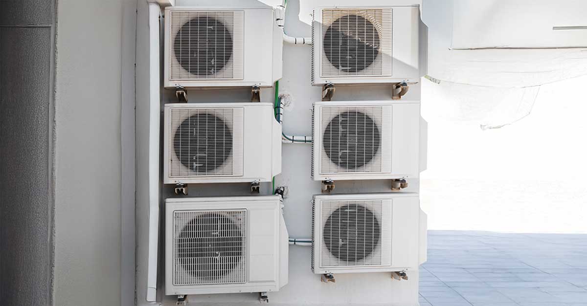 Row of six outdoor heat pump or air conditioning units mounted on a building wall for centralized cooling and heating.