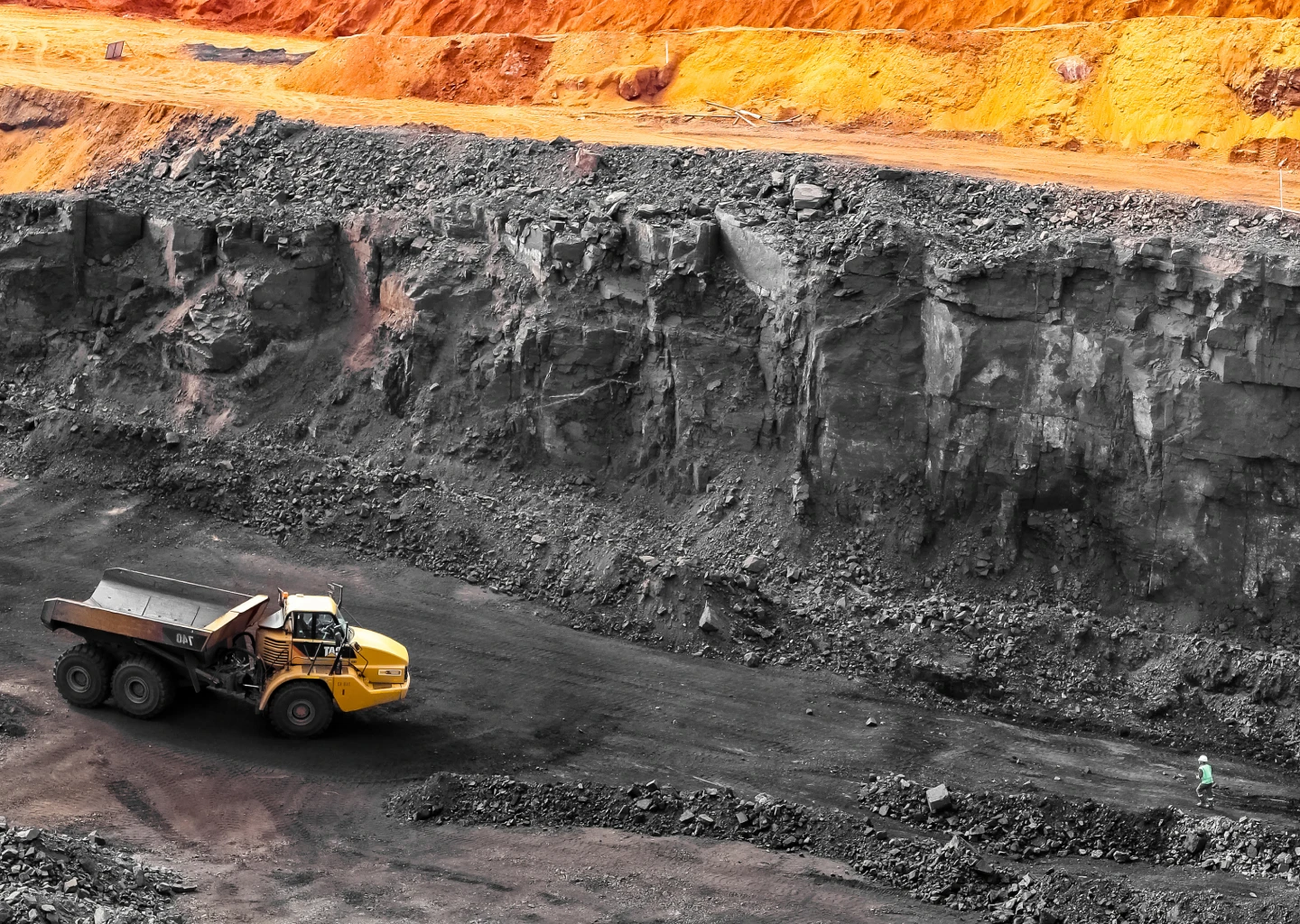 Open-pit mine with a yellow dump truck and excavator working near steep rocky walls.