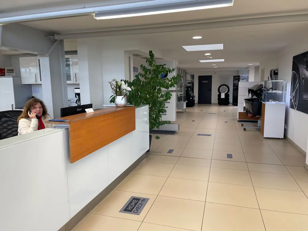 Empfangsbereich mit einer Frau, die am Telefon spricht, einem Holztresen, einer großen Pflanze und einem Gang mit Ausstellungsstücken.