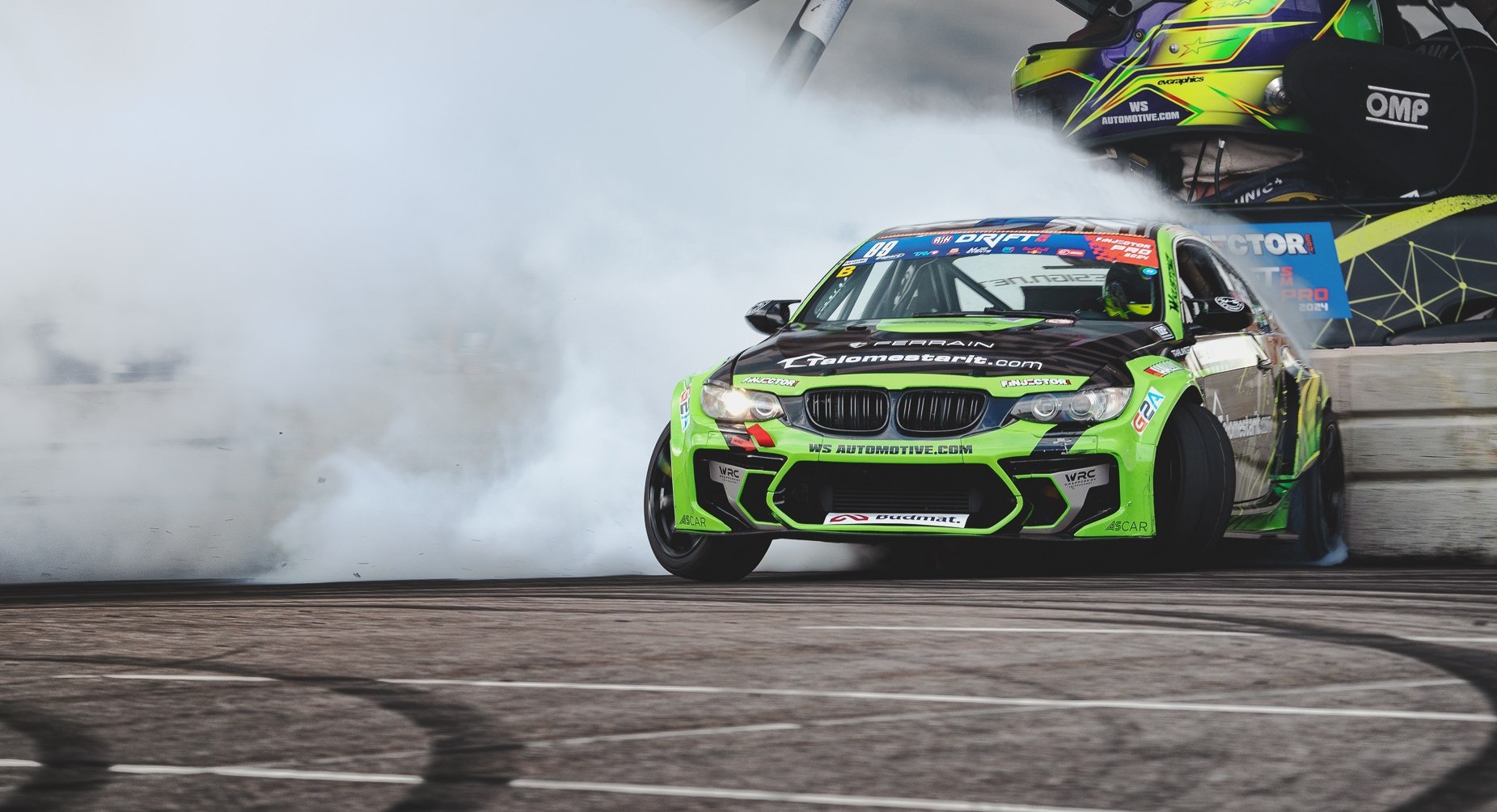 Green and black race car drifting on asphalt with smoke trailing behind.