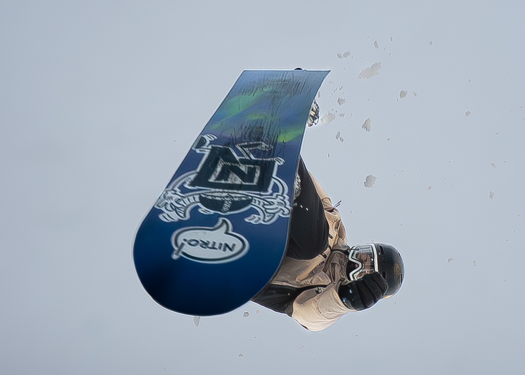 Snowboarder wearing a helmet and goggles performs an aerial trick against a gray sky.