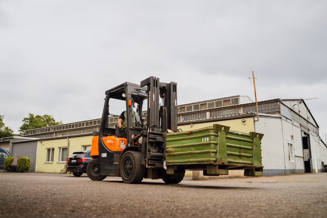 Gabelstapler transportiert einen grünen Stahlcontainer über das Betriebsgelände eines Recyclingbetriebs
