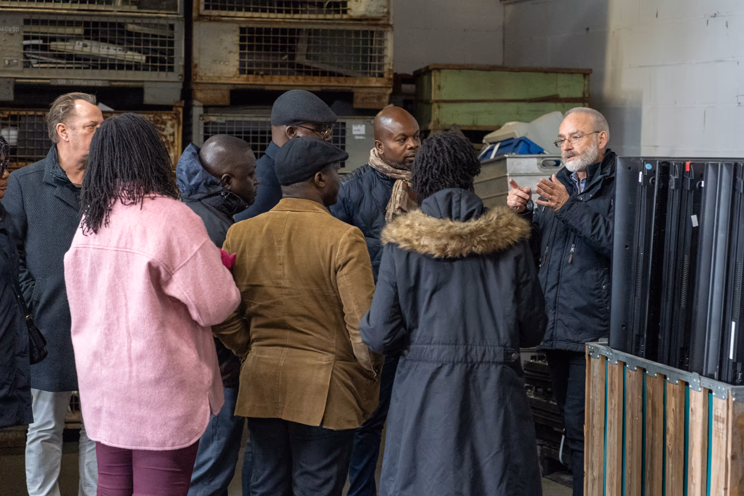 Gruppe internationaler Gäste hört einem Mann bei einer Führung durch eine Recyclinganlage aufmerksam zu