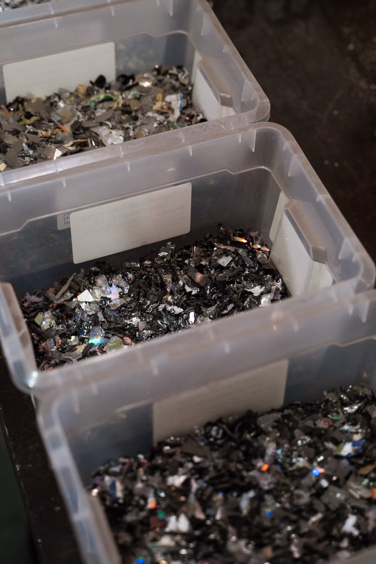 Kunststoffboxen mit sortiertem, geschreddertem Elektroschrott, darunter glänzende Metall- und Kunststofffragmente