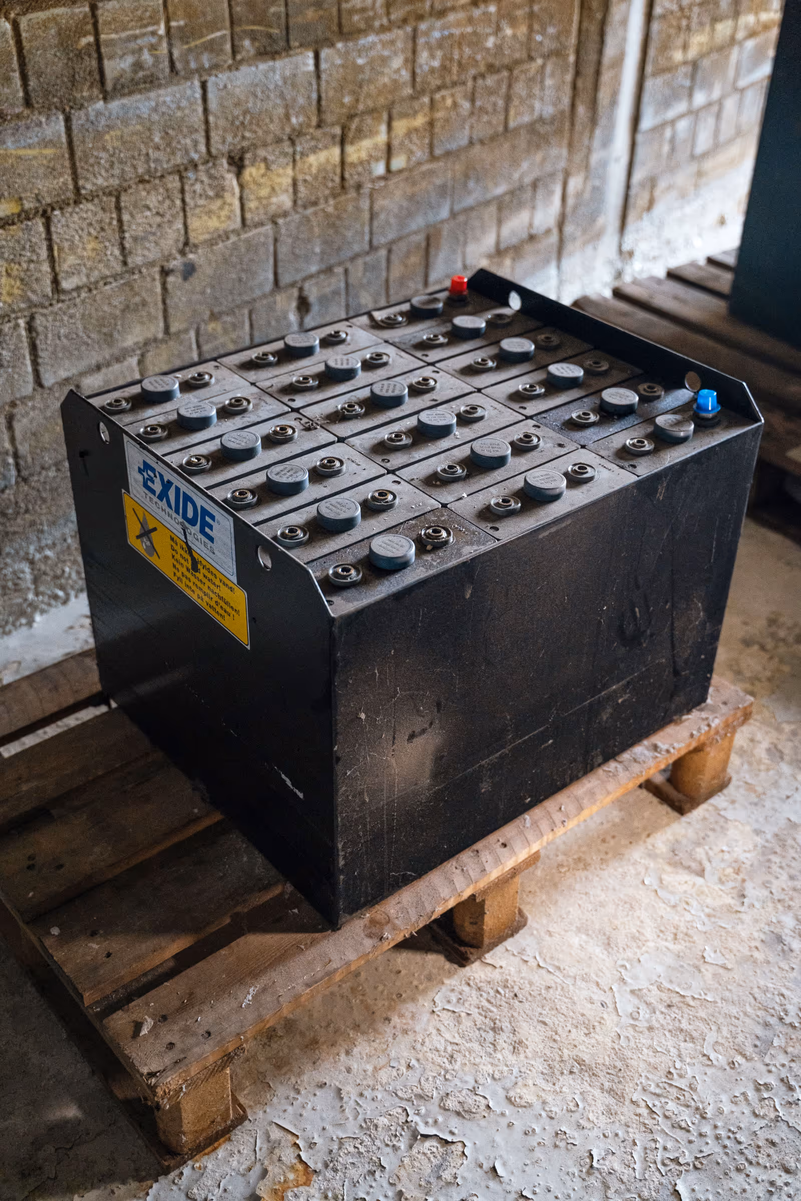 Große schwarze Industriebatterie auf einer Holzpalette, gelagert in einem Gebäude mit rohem Betonboden