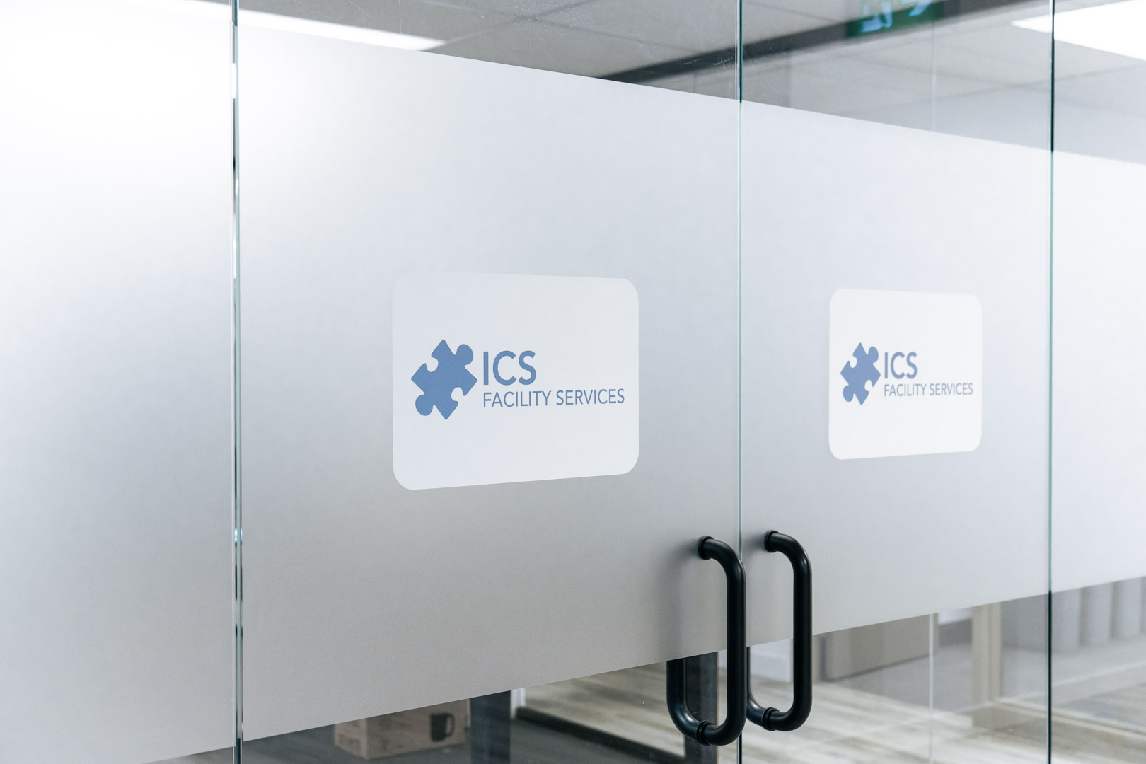 Glass doors with frosted panels and ICS Facility Services logo decals, featuring black door handles.