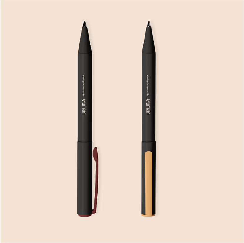 Two black makeup pencil eyeliners with pointed tips on a beige background, one with a maroon clip and the other with a beige clip.