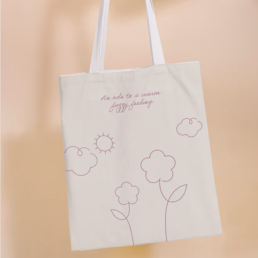 Beige tote bag with purple line drawings of clouds, sun, and flowers, and text saying 'An ode to a warm fuzzy feeling.'
